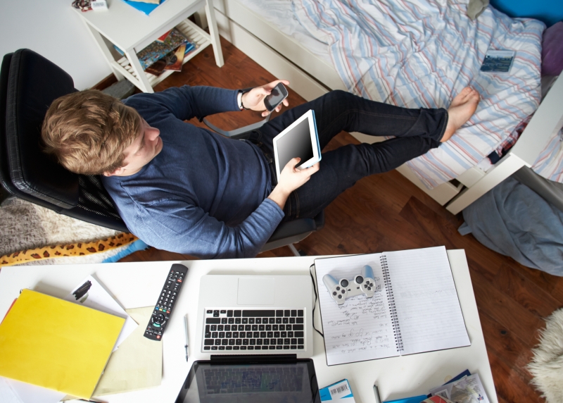 teenage-boy-using-digital-tablet-and-mobile-phone-in-bedroom